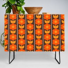 an orange and brown flowered cabinet next to a potted plant on a stand