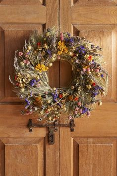 a wreath hanging on the front door of a house with dried flowers and leaves around it