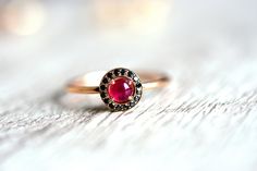 a close up of a ring with a red stone in it on a white surface