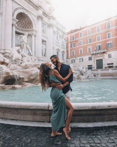 a man and woman hugging in front of a fountain