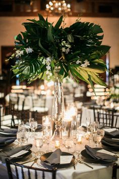 a vase filled with lots of greenery on top of a table covered in plates and silverware