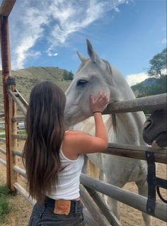 a girl petting a white horse on the nose while standing next to a fence