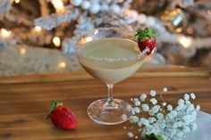 a drink in a glass with strawberries next to it on a wooden table near a christmas tree