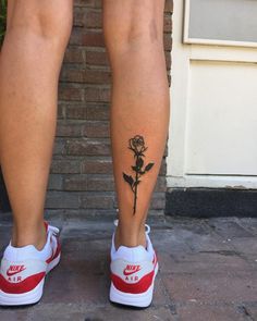 a person with a rose tattoo on their leg, standing in front of a brick wall