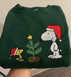 a hand holding a green christmas sweater with a dog and tree embroidered on the front