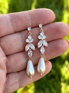 a hand holding a pair of earrings in it's left hand, with diamonds and pearls on them