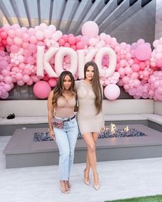 two beautiful women standing next to each other in front of pink and white balloon decorations