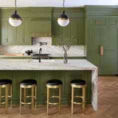 a kitchen with green cabinets and marble counter tops, gold stools at the island