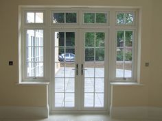 an empty room with double doors and two windows on each side, looking out onto a driveway