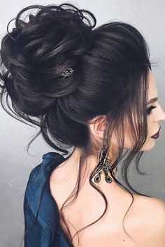 a woman with her hair in a messy updo is wearing earrings and a blue shirt