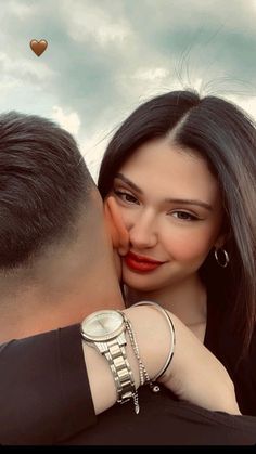 a man kissing a woman's face with a watch on her wrist and the sky in the background