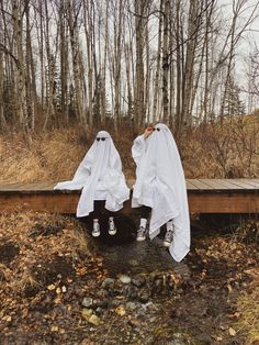 two people dressed in white are sitting on a wooden bench and one is covering his face with her hands