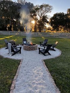 a fire pit with chairs around it in the middle of a grassy area next to a fence