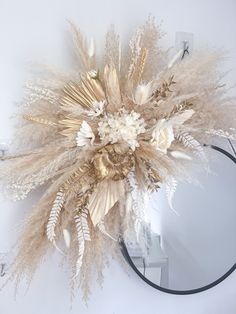 a mirror hanging on the wall with dried flowers and feathers