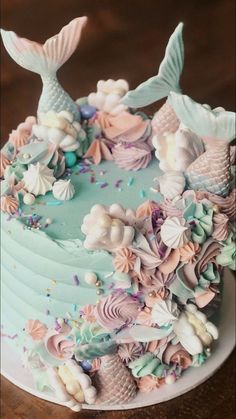 a blue cake with pink and white frosting mermaid themed decorations on the top is sitting on a wooden table