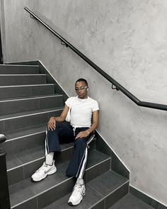 a man sitting on some stairs with his legs crossed and looking at the camera while wearing white sneakers