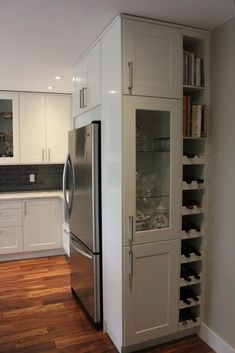 a kitchen with white cabinets and wood flooring next to a stainless steel refrigerator freezer