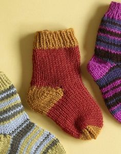 three knitted socks laying next to each other on a yellow surface with one sock in the middle