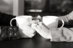 two people holding hands while sitting at a table with coffee mugs in front of them