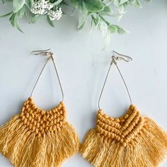 two pairs of earrings with fringes hanging from the hooks on a white surface next to flowers