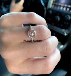 a woman's hand with a diamond ring on her finger, in front of a car