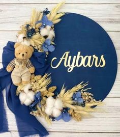 a teddy bear sitting on top of a blue wreath with the word algars