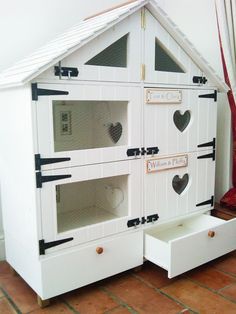 a white doll house with lots of windows and hearts on the front door, sitting on a brick floor