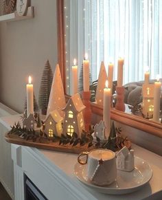 lit candles sit on a tray in front of a mirror with christmas trees and houses