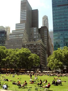 many people are sitting on the grass in front of some tall buildings and skyscrapers