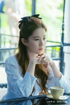 a young woman sitting at a table with a cup of coffee in her hand and looking off to the side