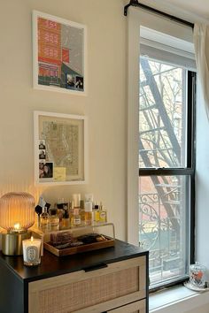 a dresser with candles and pictures on it next to a window in a living room