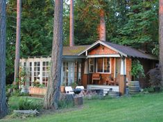 a small cabin in the middle of some trees with a picnic table and chairs outside