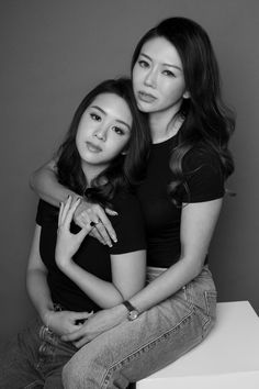 two women sitting next to each other on top of a white table and posing for the camera