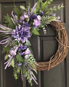 a wreath with purple flowers and greenery hanging on a door