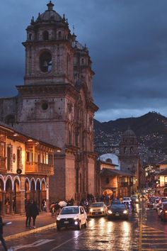 a city street filled with lots of traffic next to tall buildings and mountains in the background