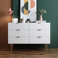 a white dresser sitting next to a green wall with a painting on top of it