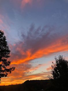 the sun is setting behind some trees and clouds in the sky, with only one cloud visible