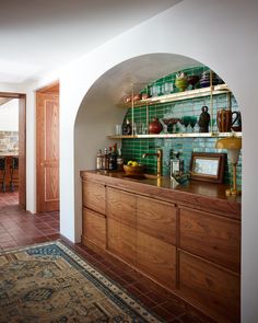 an arched doorway leads to a dining room with green tiles on the wall and wooden cabinets