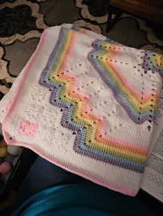 a crocheted blanket is laying next to an open book on the floor,