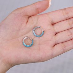 a person's hand holding two small blue and silver hoop earrings in their palm