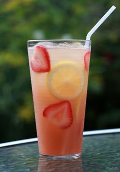 a drink with strawberries and lemon on the rim is sitting on a table outside