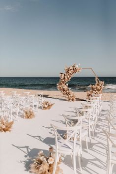 an outdoor ceremony setup with chairs and flowers on the sand at the beach in front of the ocean