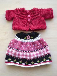 two knitted sweaters and hat sitting on top of a wooden table