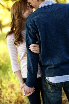 a man and woman standing next to each other in the grass with trees behind them