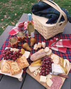 a picnic table with cheeses, crackers and grapes on it in front of a picnic basket