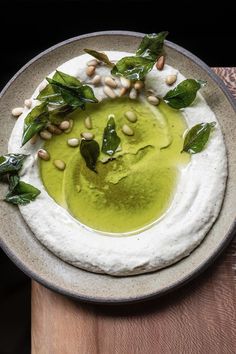 a bowl filled with hummus and greens on top of a wooden table