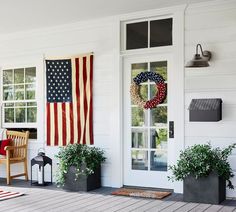 an american flag hanging on the front door of a house with potted plants and chairs