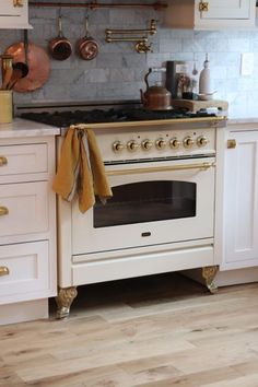 a white stove top oven sitting inside of a kitchen next to wooden floors and cabinets