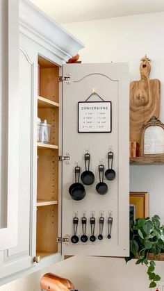 an open cabinet with pots and pans hanging on the wall next to a plant