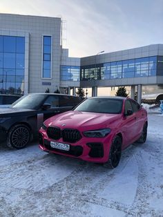 two cars parked in front of a building on snow covered ground with buildings behind them